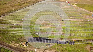 Aerial view of solar power plant under construction on green field. Assembling of electric panels for producing clean