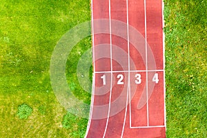Aerial view of sports stadium with red running tracks with numbers on it and green grass football field
