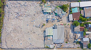 Aerial view of stack of different types of large garbage pile, plastic bags, and trash with a tractor car in industrial factory in