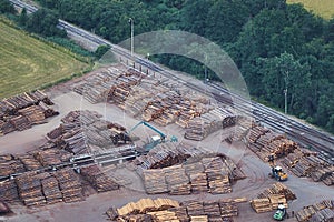 Aerial view of stacked lumber piles with heavy moving machinery and a railway track.