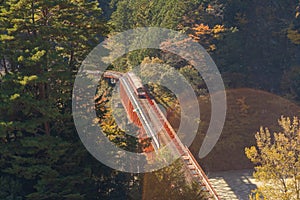 Aerial view of the steam train crossing Oigawa Railroad to go to station with red fall foliage in forest mountain hills and blue