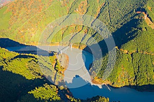 Aerial view of the steam train crossing Oigawa Railroad to go to station with red fall foliage in forest mountain hills and blue