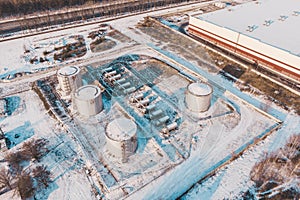 Aerial view of steel or metal storage tanks for oil or fuel near industrial warehouse or factory building in winter