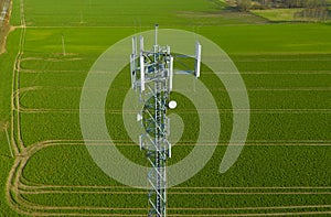 Aerial view on steel telecommunication tower in the middle of green field transmitting radio, telephone and internet signal