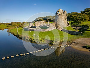 Aerial view of stepping stones over a small river leading to the ruins of an ancient castle Ogmore Castle, Wales
