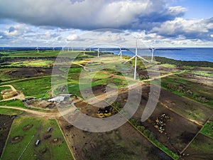 Aerial view of stormy clouds above wind turbines and pastures on ocean shore.