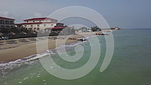 Aerial view of straw umbrellas on the beach. Ocean waves washing sandy shore. Tranquil coast line of a luxury resort.