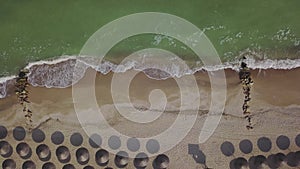 Aerial view of straw umbrellas on the beach. Ocean waves washing sandy shore. Tranquil coast line of a luxury resort