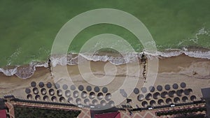 Aerial view of straw umbrellas on the beach. Ocean waves washing sandy shore. Tranquil coast line of a luxury resort.