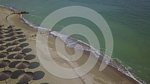 Aerial view of straw umbrellas on the beach. Ocean waves washing sandy shore. Tranquil coast line of a luxury resort.