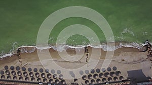 Aerial view of straw umbrellas on the beach. Ocean waves washing sandy shore. Tranquil coast line of a luxury resort.