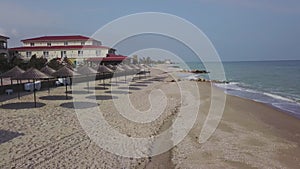 Aerial view of straw umbrellas on the beach. Ocean waves washing sandy shore. Tranquil coast line of a luxury resort.