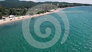 Aerial view of stunning blue beach below a hill in the area of Halkidiki Greece, move forward and down by drone