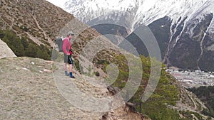 Aerial view of a stylish young man in a sunglasses cap and shorts with a jacket walks trekking with sticks along the
