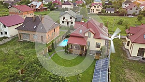 Aerial view of suburban homes and private house with green grass covered yard, solar panels on roof, swimming pool with blue water