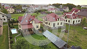Aerial view of suburban homes and private house with green grass covered yard, solar panels on roof, swimming pool with blue water