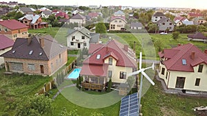 Aerial view of suburban homes and private house with green grass covered yard, solar panels on roof, swimming pool with blue water