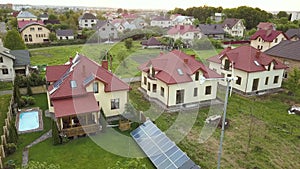 Aerial view of suburban homes and private house with green grass covered yard, solar panels on roof, swimming pool with blue water