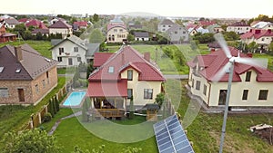 Aerial view of suburban homes and private house with green grass covered yard, solar panels on roof, swimming pool with blue water