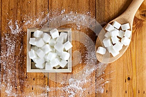 Aerial View of Sugar Cubes in Square Shaped Bowl and Spoon with Unrefined Sugar spill over in Wooden Background. photo