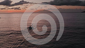 Aerial view of sunrise above ocean with dark silhouettes of fishing boat going for fishery. Sea water reflecting morning