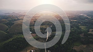 Aerial view sunrise over countryside, hills are covered with brown grass backlit. Green trees summer