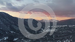 The Aerial view of a sunset over mountain in Arahova, Greece, a view of the valley below with trees covered by snow