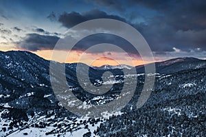 The Aerial view of a sunset over mountain in Arahova, Greece, a view of the valley below with trees covered by snow