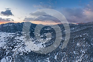The Aerial view of a sunset over mountain in Arahova, Greece, a view of the valley below with trees covered by snow