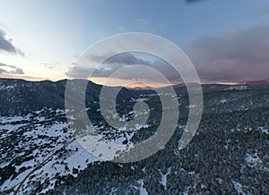 The Aerial view of a sunset over mountain in Arahova, Greece, a view of the valley below with trees covered by snow