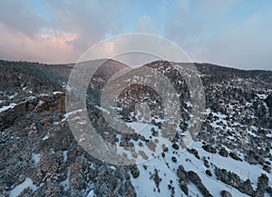 The Aerial view of a sunset over mountain in Arahova, Greece, a view of the valley below with trees covered by snow