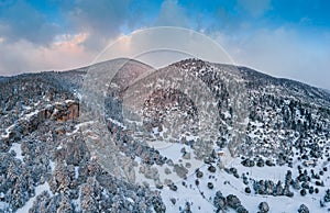 The Aerial view of a sunset over mountain in Arahova, Greece, a view of the valley below with trees covered by snow