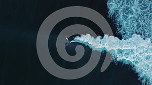 Aerial view of a surfer catching a wave as he curves down. The swell has arrived