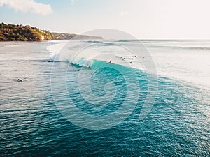 Aerial view with surfers and turquoise barrel wave in ocean.