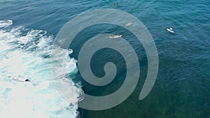 Aerial view of surfers waiting and paddling to the waves in blue water