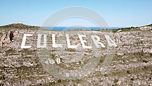 Aerial view surrounding the large sign painted on the Sierra de los Zorros mountain with the name of Cullera, in the province of