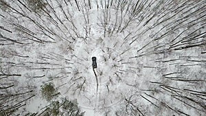 Aerial view on SUV 6x6 that rides by snow-covered road in winter forest, top view