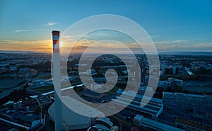 Aerial view of tall chimney of thermal power plant against setting sun.