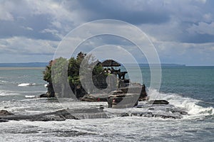 Aerial view of Tanah Lot temple on cliff in Indian ocean. Waves are breaking on a rock cliff off the coast of Bali. Hindu temple