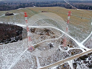Aerial view telecommunication towers of mobile communication on the background of green field is covered with white snow.