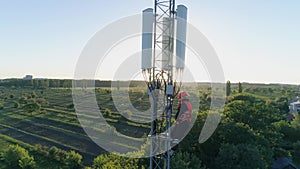 Aerial view of telecommunications tower, technician in safety vest and hard hat uses mobile phone on top of cellular