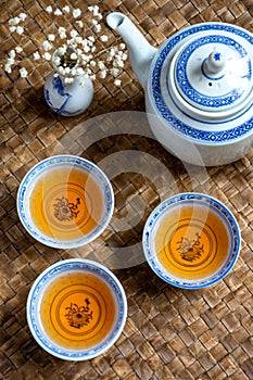 Aerial view of three blue teacups with teapot, white flowers, selective focus, on braided tray