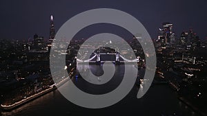 Aerial view to the illuminated Tower Bridge and skyline of London, UK at night.