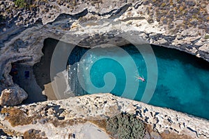 Aerial view to the Papafragas cave beach with a woman floating over turquoise waters, Milos island, Greece