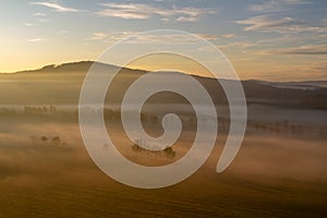 Aerial view to trees silhouette in misty orange fog at sunrise, Czech landscape