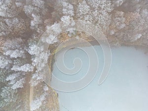 Aerial view or top view of winter forest lake, showing the ice on the lake and the pine trees with snow covered. Winter