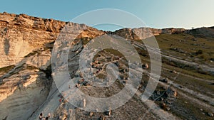 Aerial view of touristic group of people walking around white giant cliff on blue clear sky background. Shot. Exploring