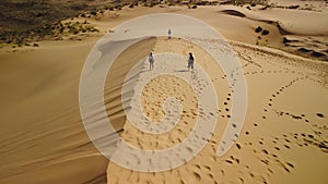Aerial view tourists woman and man drone pilot walking golden sand dunes top
