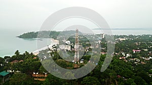 Aerial view of a towering cell site on a lush island with dense greenery, surrounded by turquoise sea waters, vital for