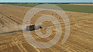 Aerial view of tractor as pulling trailer full with round bales of straw